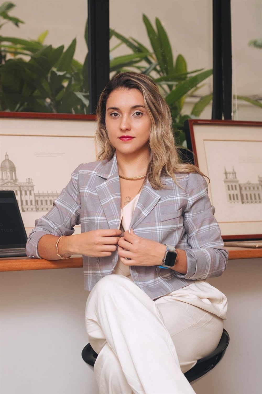 Nathalia Mancini de blazer, sentada em seu espaço de trabalho